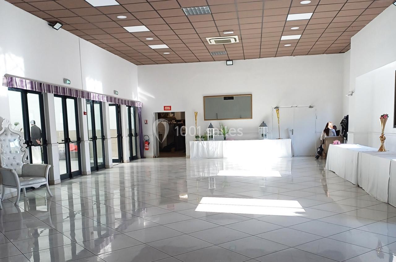 Salle lumineuse avec carrelage blanc, grandes baies vitrées, tables décorées et plafond à dalles marron.