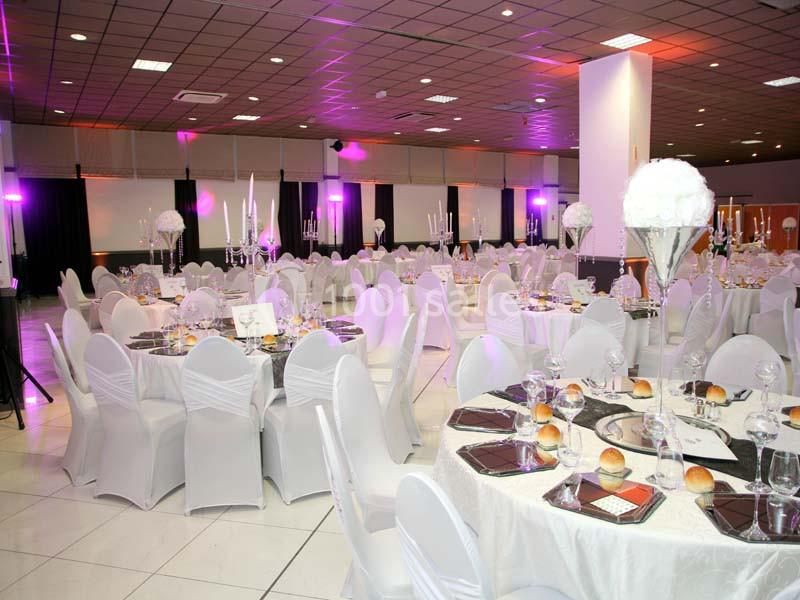 Salle de réception décorée avec des tables rondes, nappes blanches, chaises assorties et éclairage tamisé.