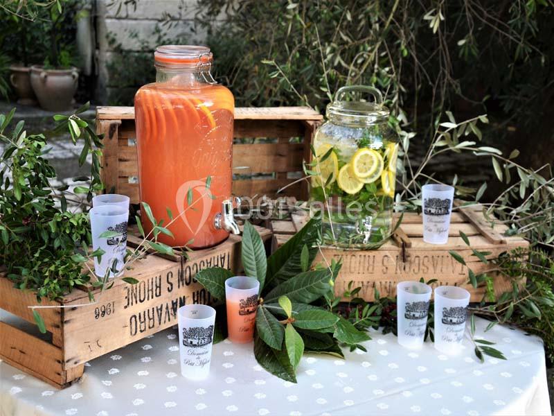 Deux jarres en verre contenant des boissons, entourées de verdure et de gobelets, disposées sur des caisses en bois.