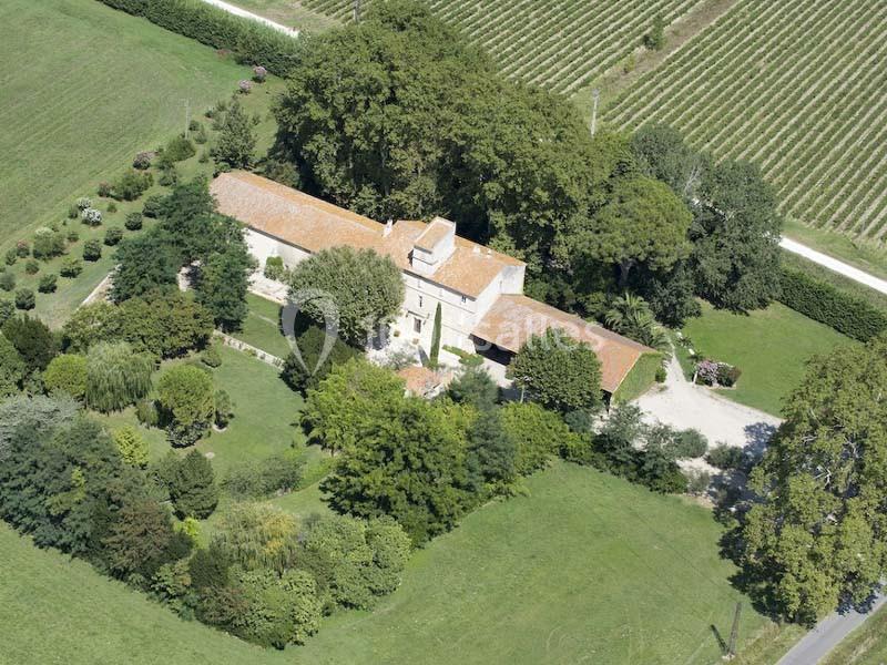 Vue aérienne d'une maison en pierre avec toit en tuiles, entourée d'un jardin arboré et de vignes.