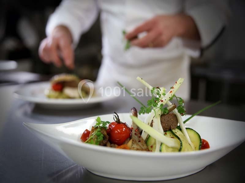 Un chef dresse des assiettes avec des légumes frais et des herbes dans une cuisine professionnelle.