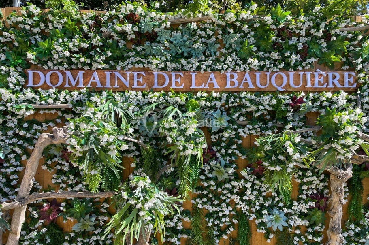 Mur végétal décoratif avec des plantes vertes et fleurs blanches, portant une enseigne ’Domaine de la Bauquière’.
