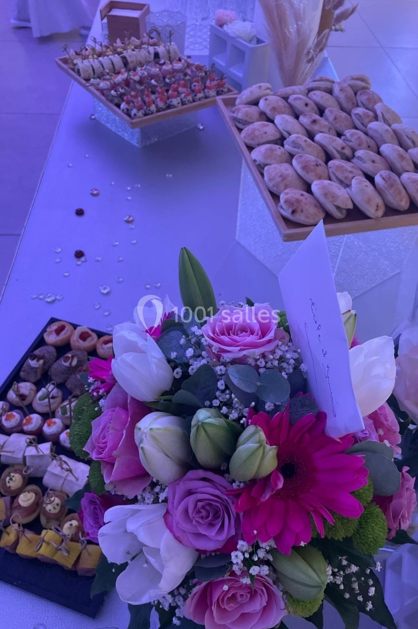 Bouquet de fleurs roses et blanches au premier plan, avec une table garnie de pâtisseries en arrière-plan.