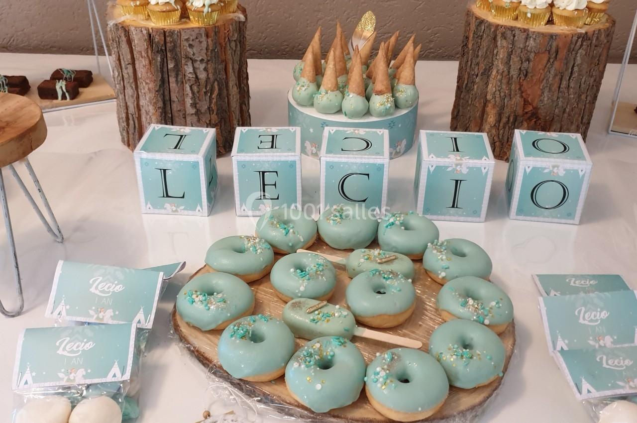 Table décorée pour une fête avec des donuts glacés bleus, des cubes décoratifs et des desserts variés sur des supports en…