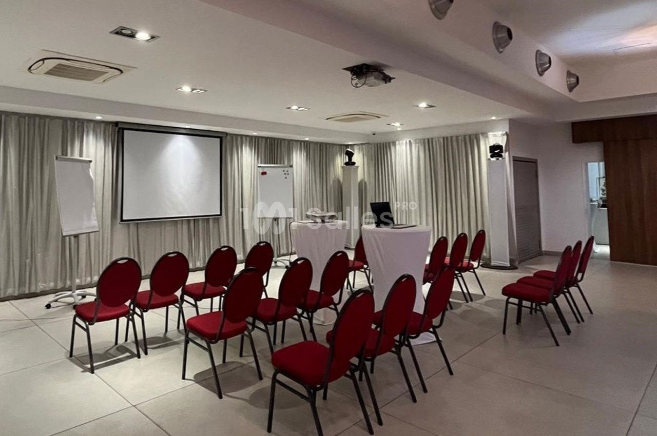 Salle de conférence avec chaises rouges disposées en rangées face à un écran de projection et un tableau blanc.