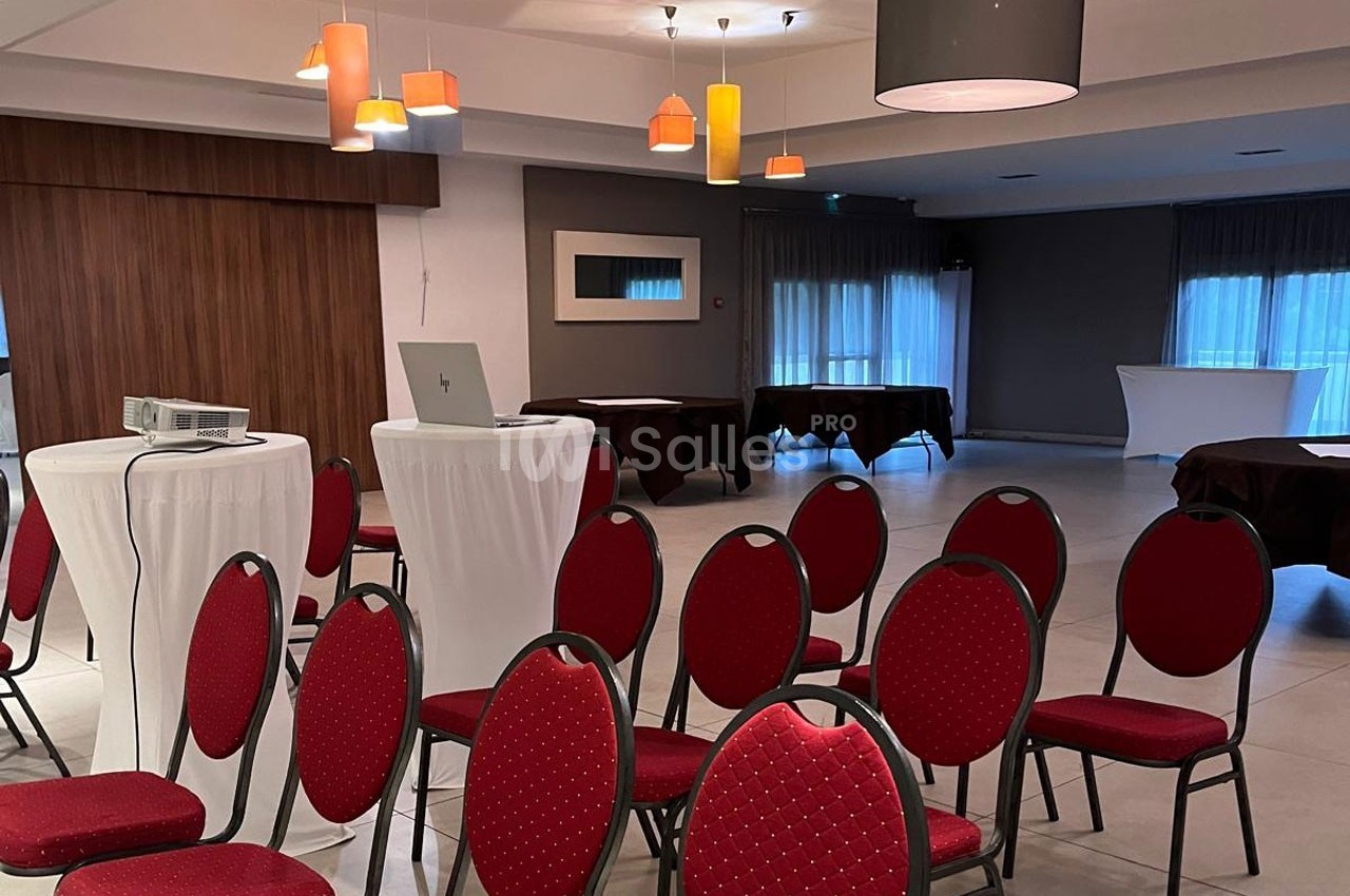 Salle de réunion avec chaises rouges, tables hautes, projecteur et éclairage suspendu.