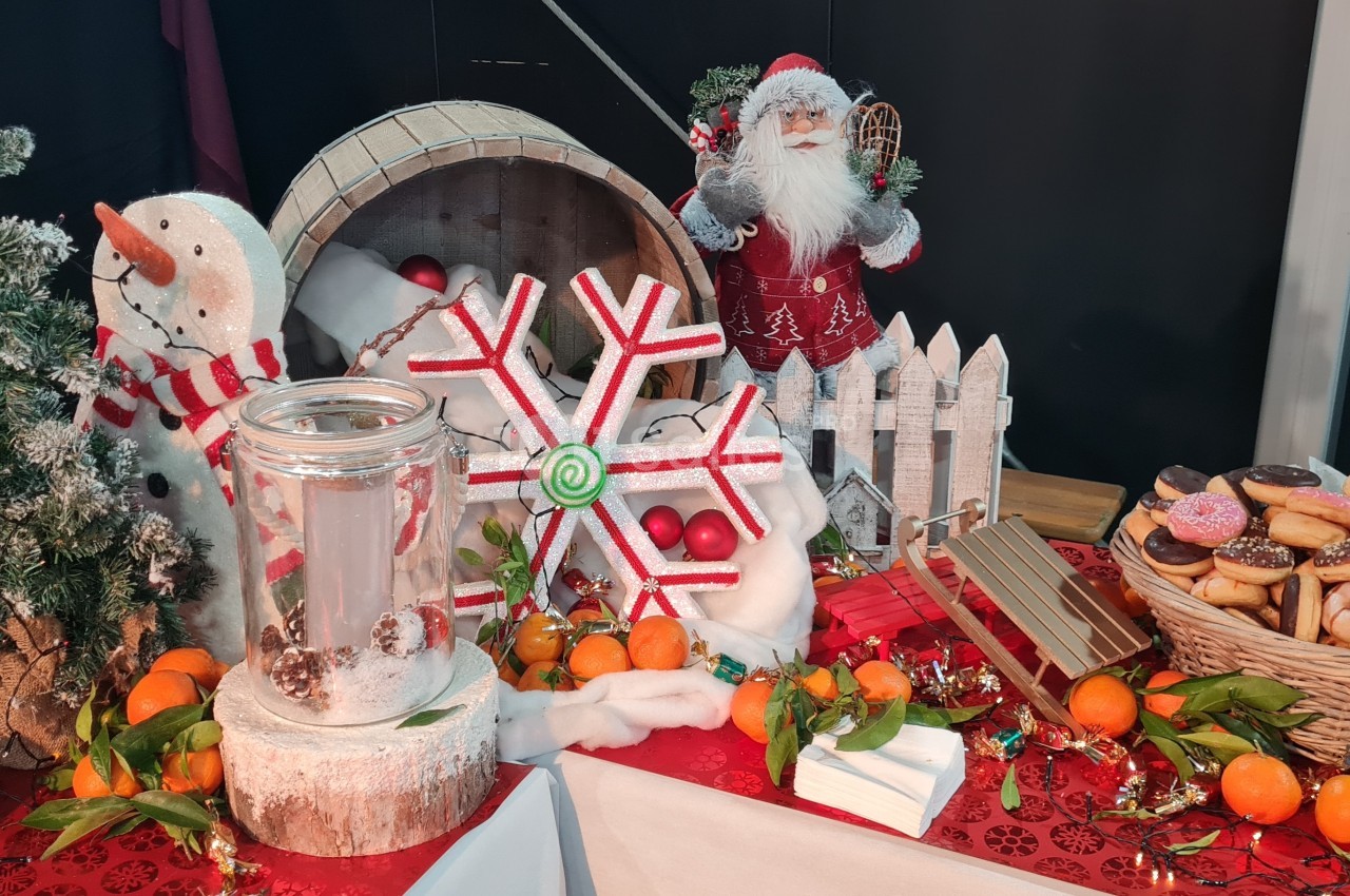 Décoration festive avec bonhomme de neige, Père Noël, paniers de fruits, beignets et ornements sur une table rouge.
