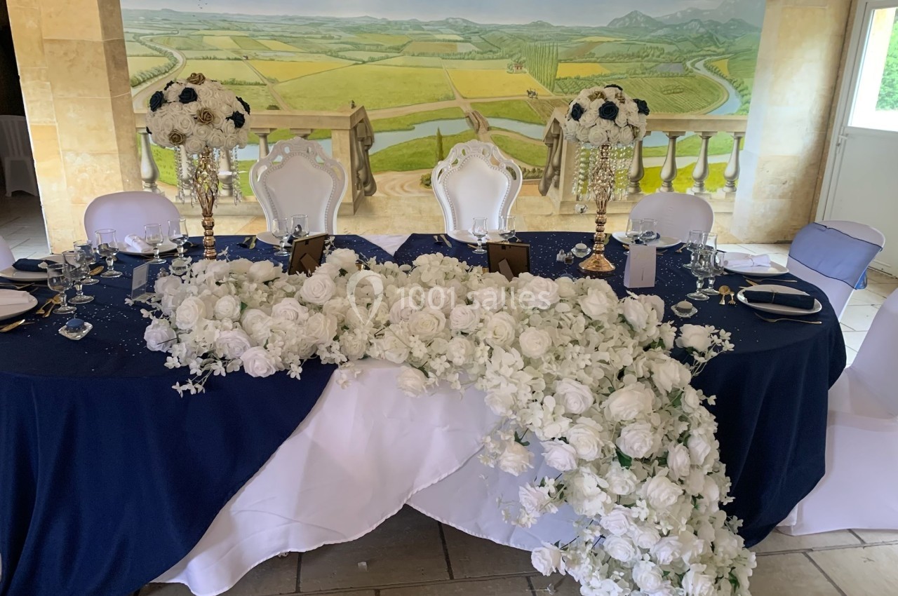 Table de réception décorée de nappes bleues et blanches, ornée de fleurs blanches et de chandeliers dorés.
