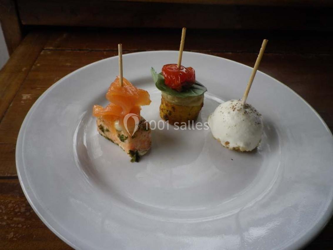 Assiette contenant trois amuse-bouches sur piques : saumon, légumes et mozzarella, présentés sur une table en bois.