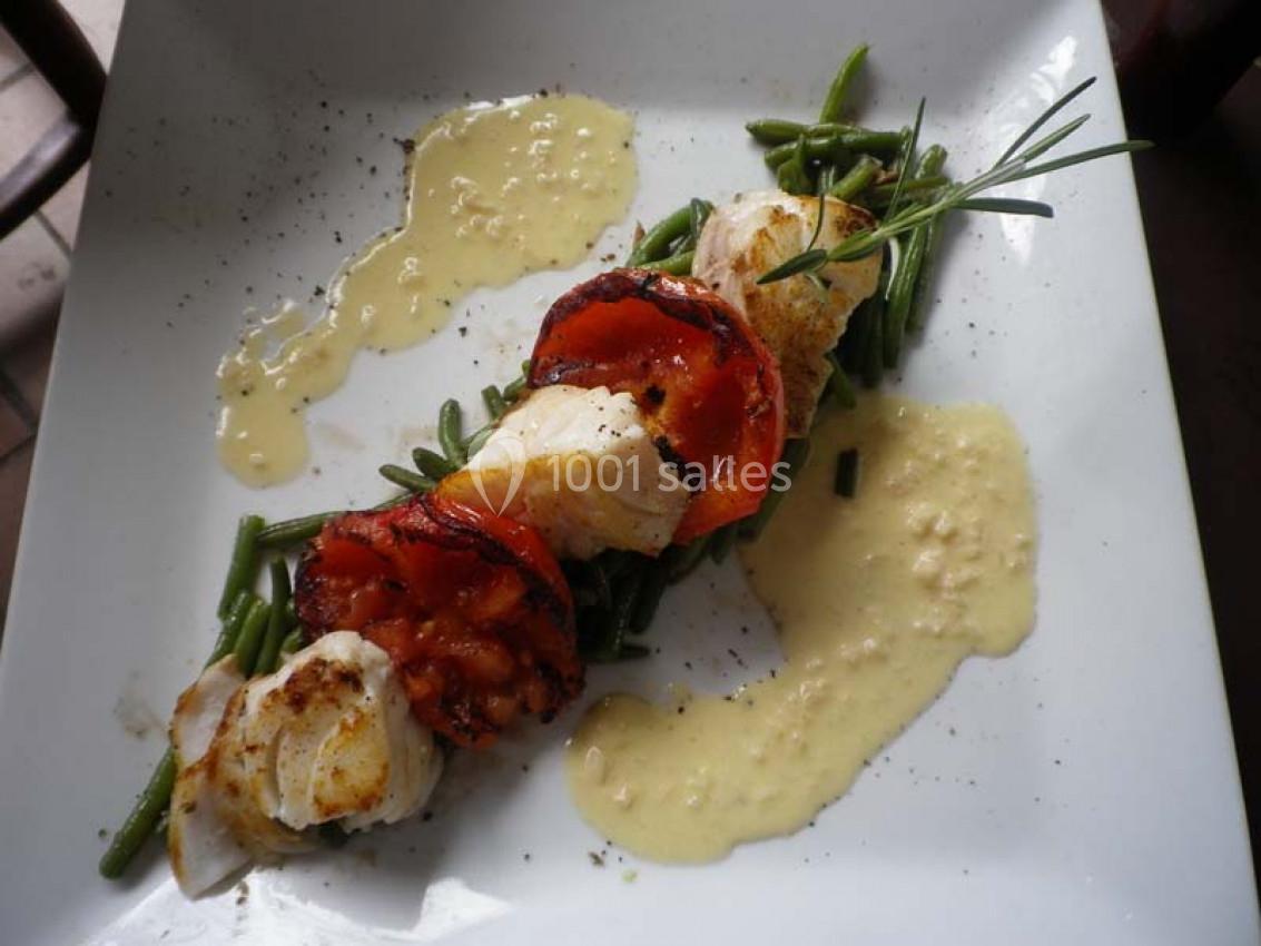 Filet de poisson grillé avec tomates, haricots verts et sauce crémeuse, présenté sur une assiette blanche.