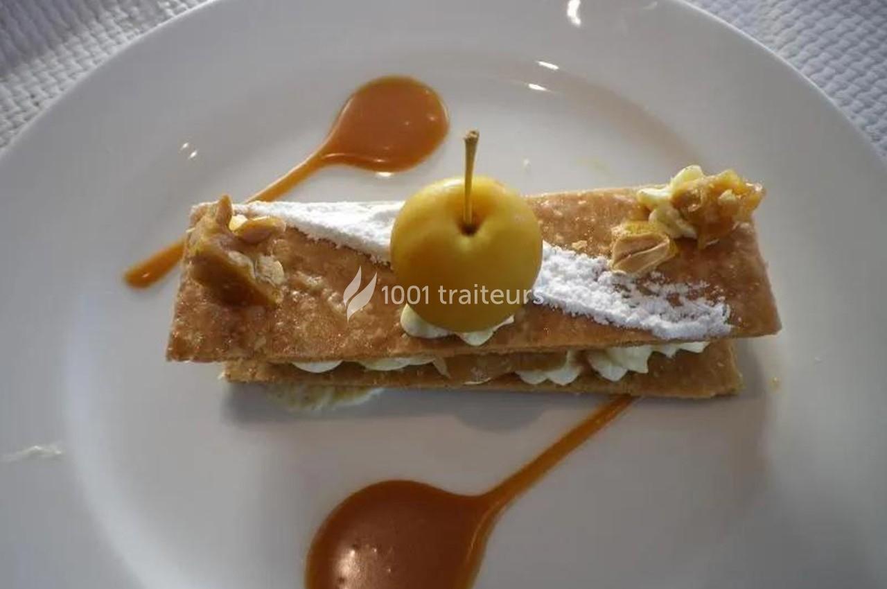 Dessert composé de couches de pâte feuilletée, crème, pomme décorative et sauce caramel sur une assiette blanche.