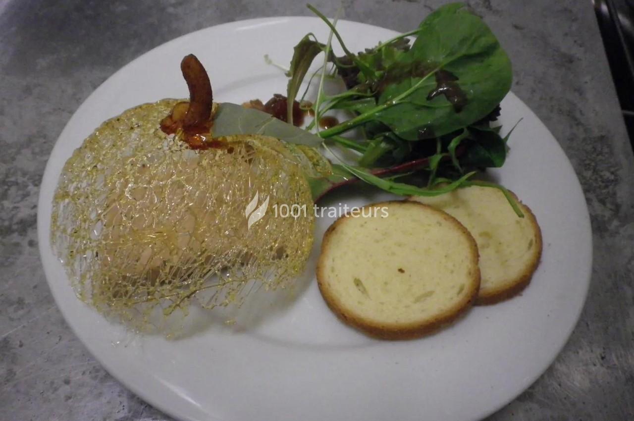 Assiette contenant un foie gras décoré de caramel filé, accompagné de toasts et d'une salade verte.