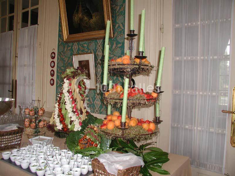 Table décorée avec des fruits, des bougies vertes sur un présentoir à étages et des verrines disposées en rangées.