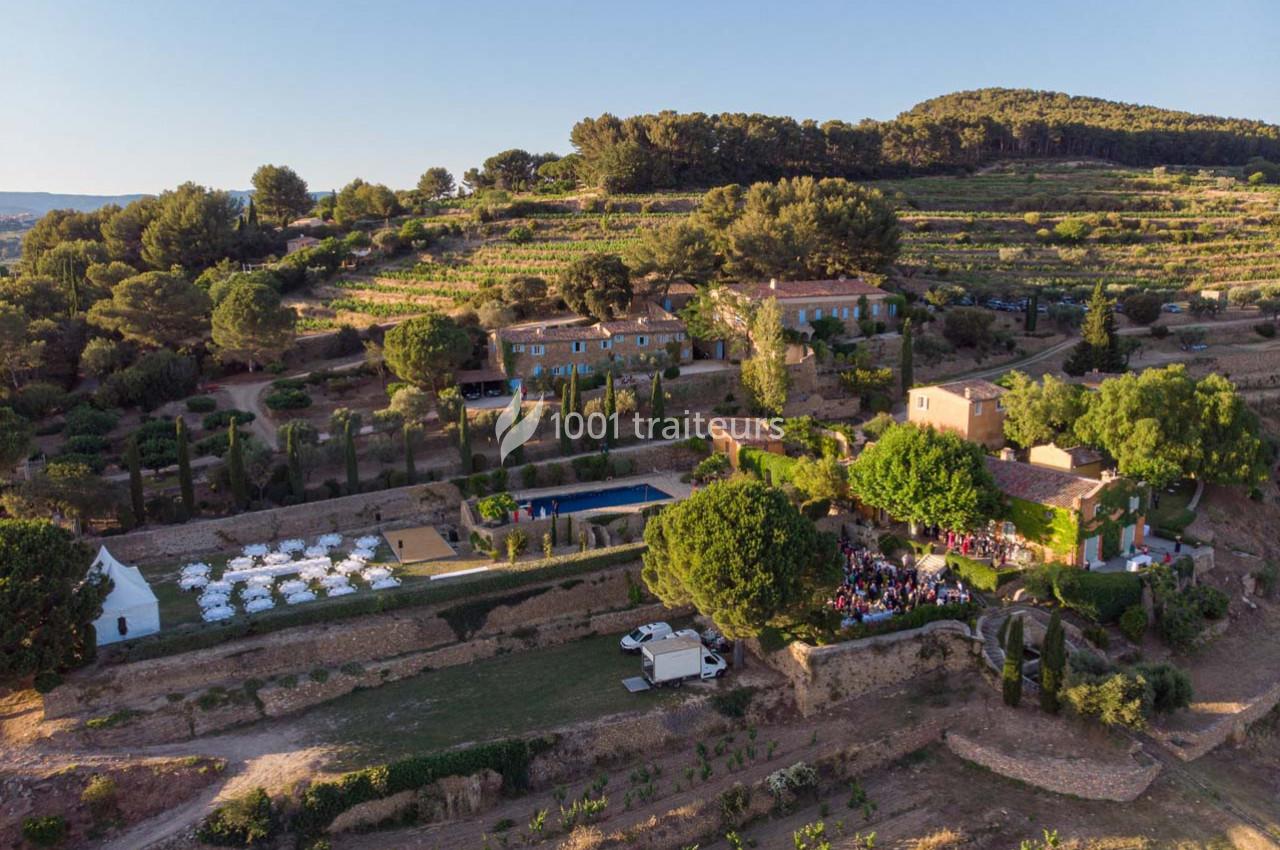 Vue aérienne d'un domaine avec bâtiments en pierre, jardins, piscine et vignobles entourés de collines verdoyantes.