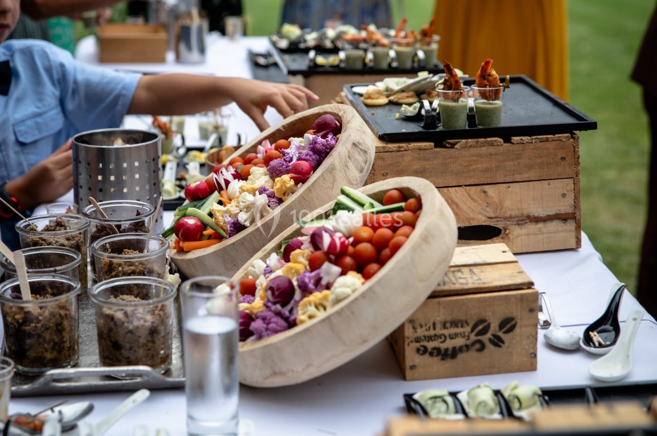 Buffet en plein air avec légumes colorés, verrines et amuse-bouches disposés sur une table blanche.