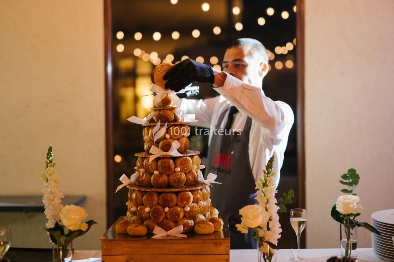 Un serveur assemble une pièce montée de choux décorée de rubans blancs, entourée de fleurs et de lumières.