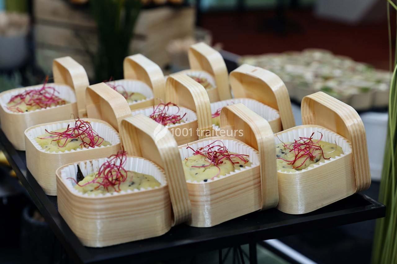 Petits plats en barquettes en bois contenant une préparation garnie de pousses rouges, présentés sur une table.