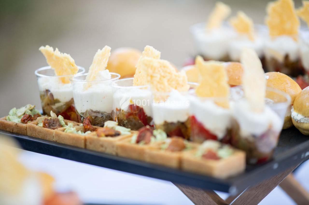 Plateau de verrines garnies de légumes, crème et tuiles de fromage, accompagné de bouchées salées sur une table.