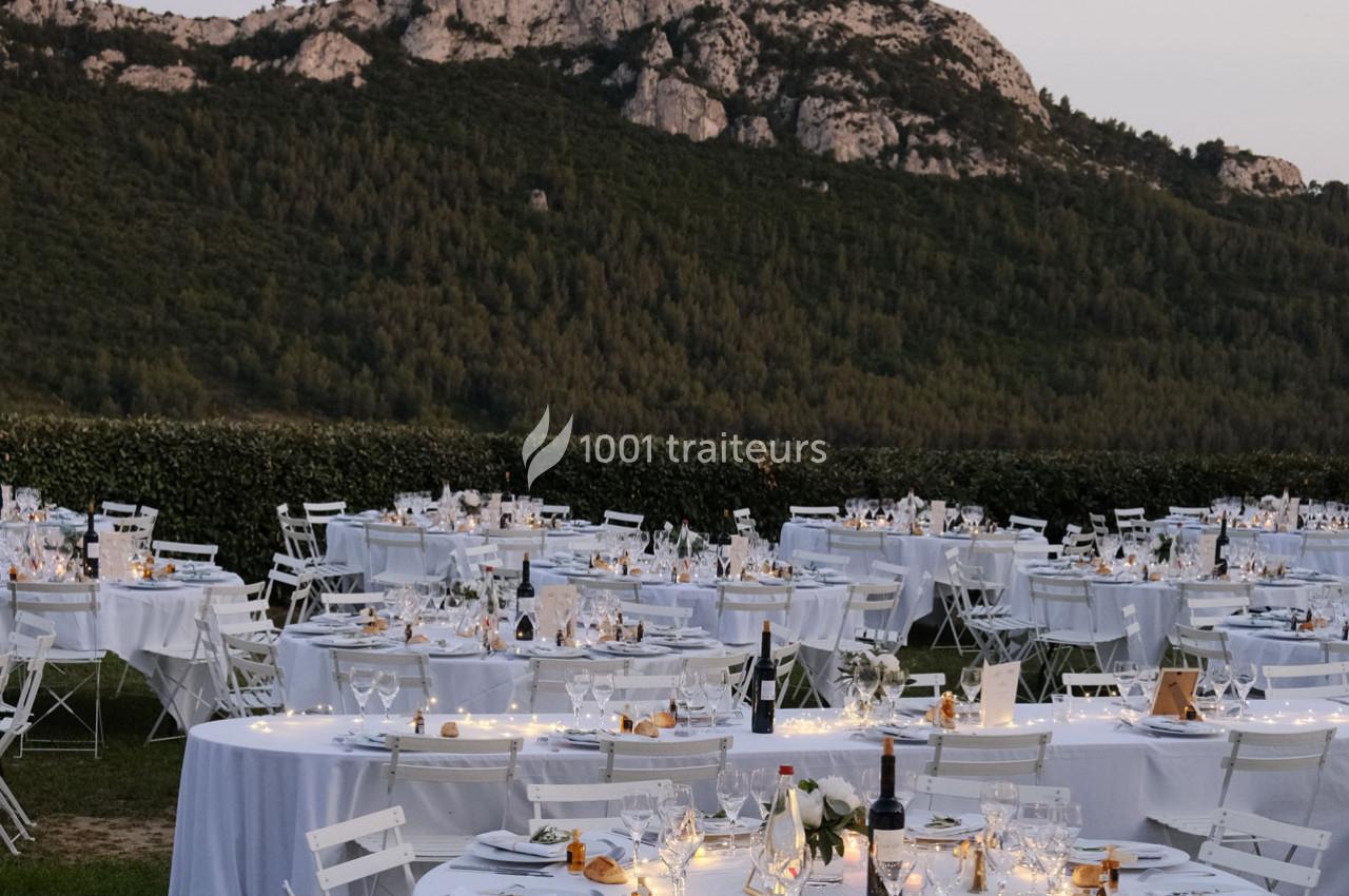 Tables rondes décorées pour un dîner en plein air, disposées sur une pelouse avec une montagne en arrière-plan.