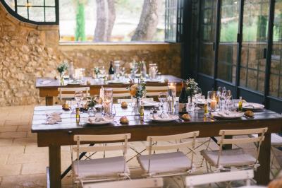 Une mariée en robe blanche tient un bouquet dans une salle décorée pour un mariage, avec un homme en costume bleu derrière…