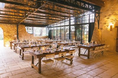 Une mariée en robe blanche tient un bouquet dans une salle décorée pour un mariage, avec un homme en costume bleu derrière…
