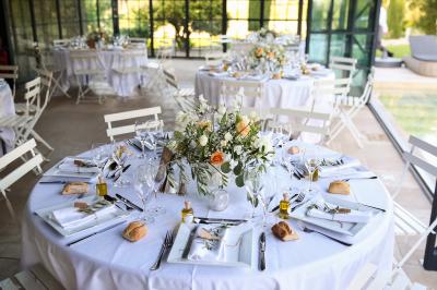Une mariée en robe blanche tient un bouquet dans une salle décorée pour un mariage, avec un homme en costume bleu derrière…