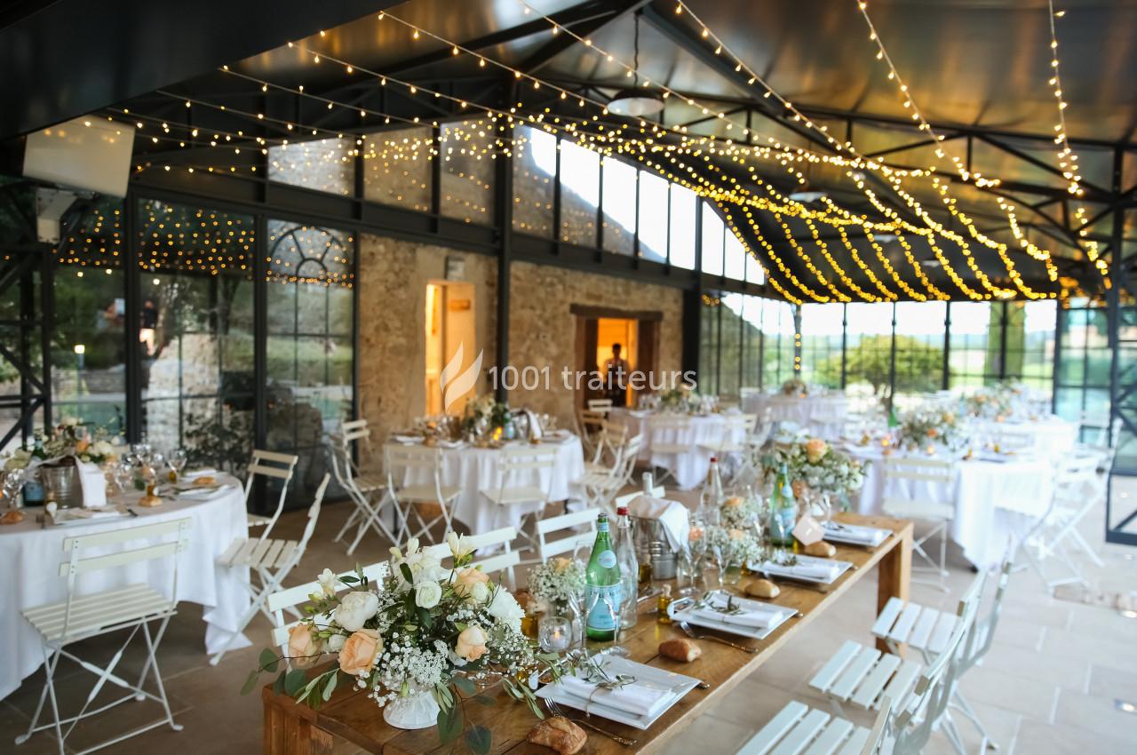 Salle de réception lumineuse décorée pour un mariage, avec tables dressées et guirlandes lumineuses suspendues.