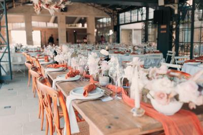 Une mariée en robe blanche tient un bouquet dans une salle décorée pour un mariage, avec un homme en costume bleu derrière…