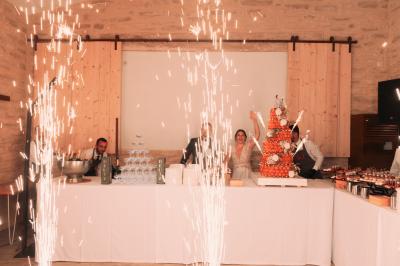 Une mariée en robe blanche tient un bouquet dans une salle décorée pour un mariage, avec un homme en costume bleu derrière…