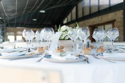 Une mariée en robe blanche tient un bouquet dans une salle décorée pour un mariage, avec un homme en costume bleu derrière…