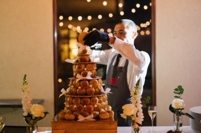 Une mariée en robe blanche tient un bouquet dans une salle décorée pour un mariage, avec un homme en costume bleu derrière…