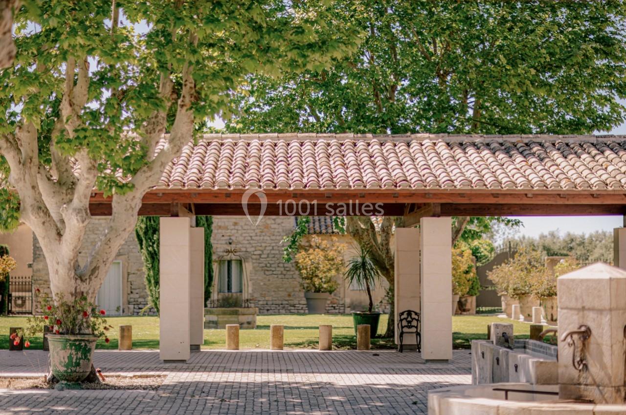 Location salle Marsillargues (Hérault) - Le Mas Saint Gabriel #3 Cour extérieure avec toit en tuiles, arbres ombrageants, pavés au sol et bâtiments en pierre en arrière-plan.