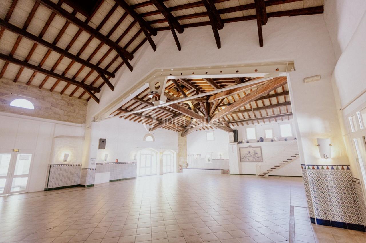 Location salle Marsillargues (Hérault) - Le Mas Saint Gabriel #7 Grande salle lumineuse avec plafond en poutres apparentes, murs blancs, carrelage au sol et escaliers sur le côté.