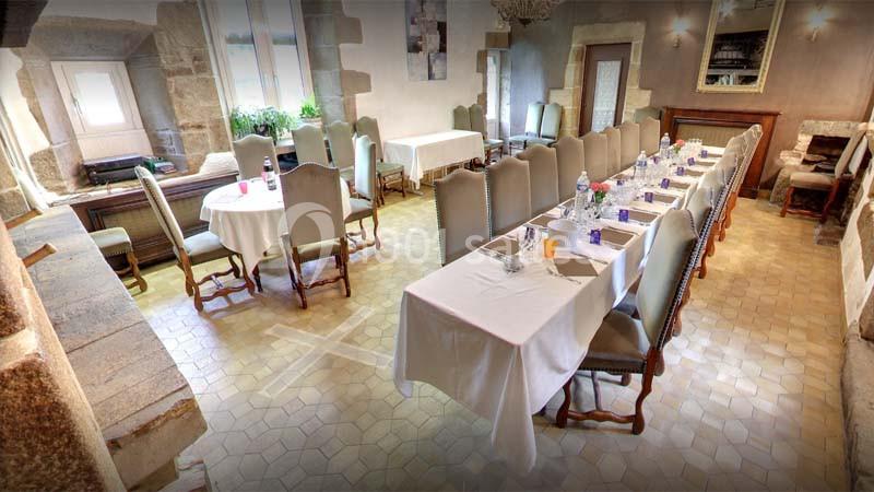 Salle de réception lumineuse avec tables dressées, chaises en bois et pierre apparente sur les murs.