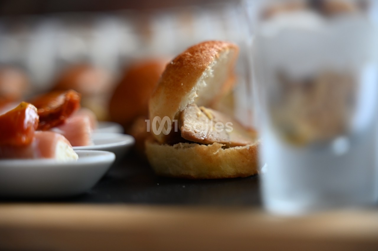 Petit pain garni de foie gras, entouré de verrines et d'amuse-bouches sur une table de présentation.