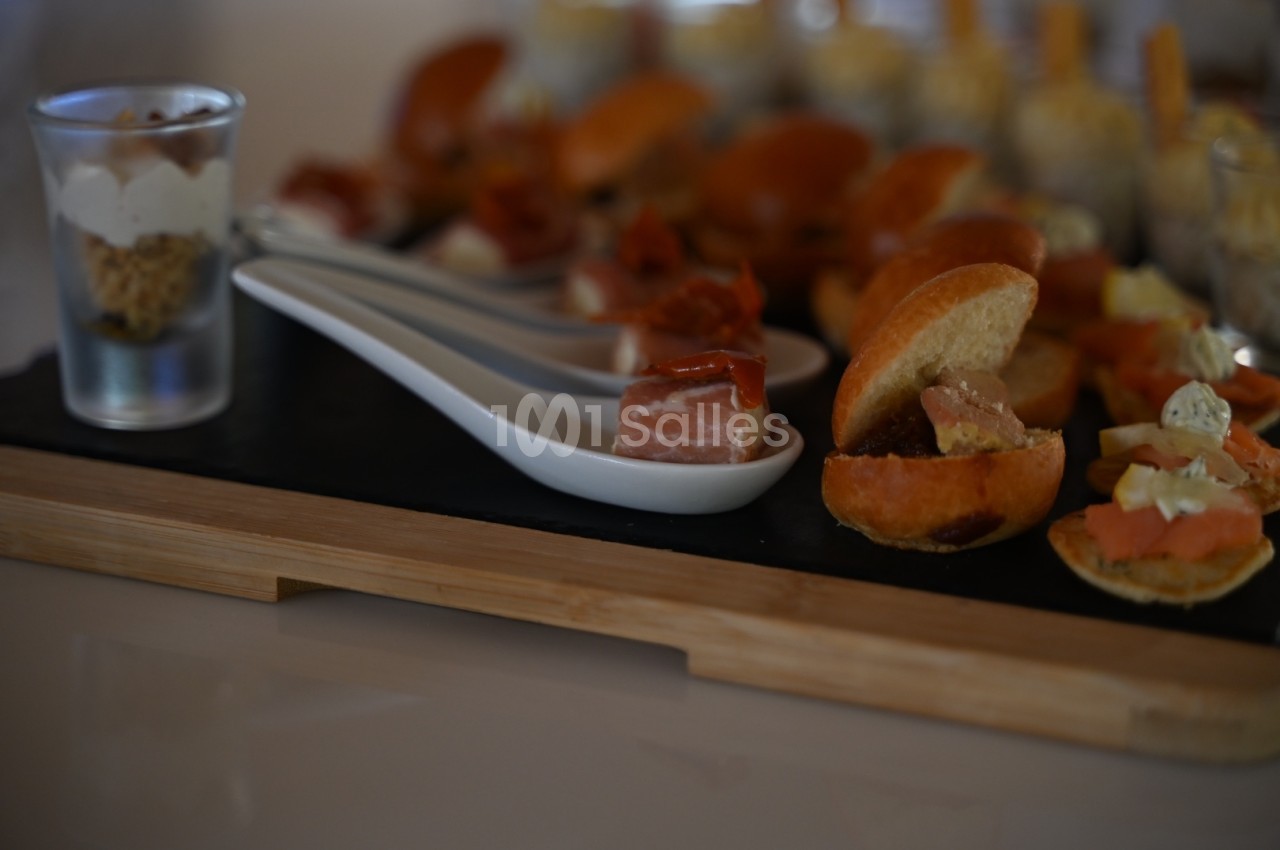Plateau de bouchées apéritives variées comprenant verrines, charcuterie et mini-sandwichs sur une planche en bois.