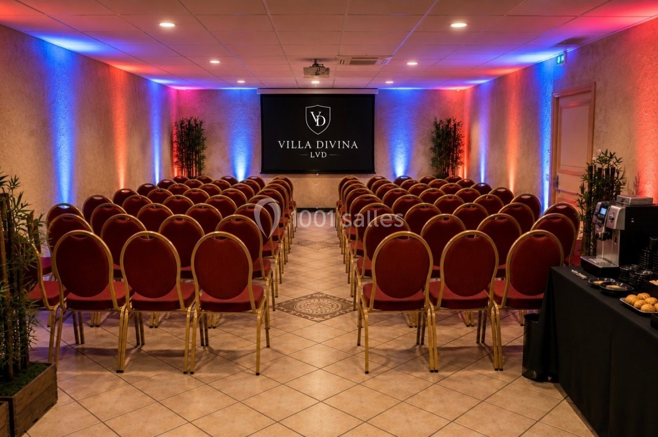 Salle de conférence avec rangées de chaises rouges, écran de projection, éclairage coloré et table de collation à droite.
