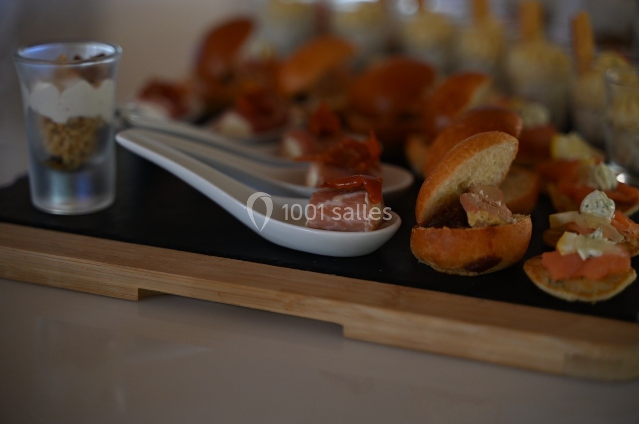 Plateau de dégustation avec verrines, cuillères garnies de charcuterie et mini-sandwichs sur une planche en bois.