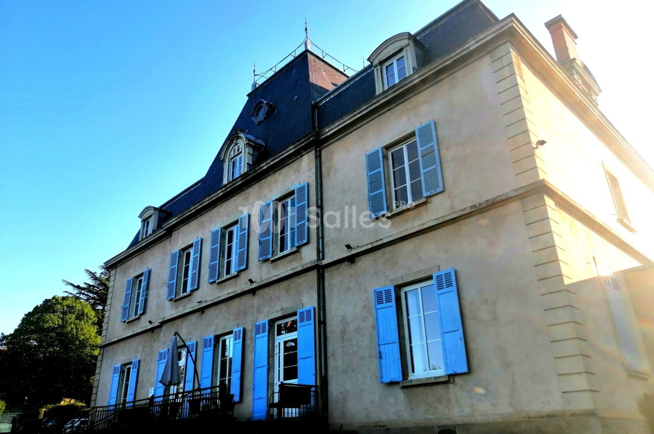 Façade d'un grand bâtiment ancien avec des volets bleus, un toit mansardé et un ciel dégagé en arrière-plan.
