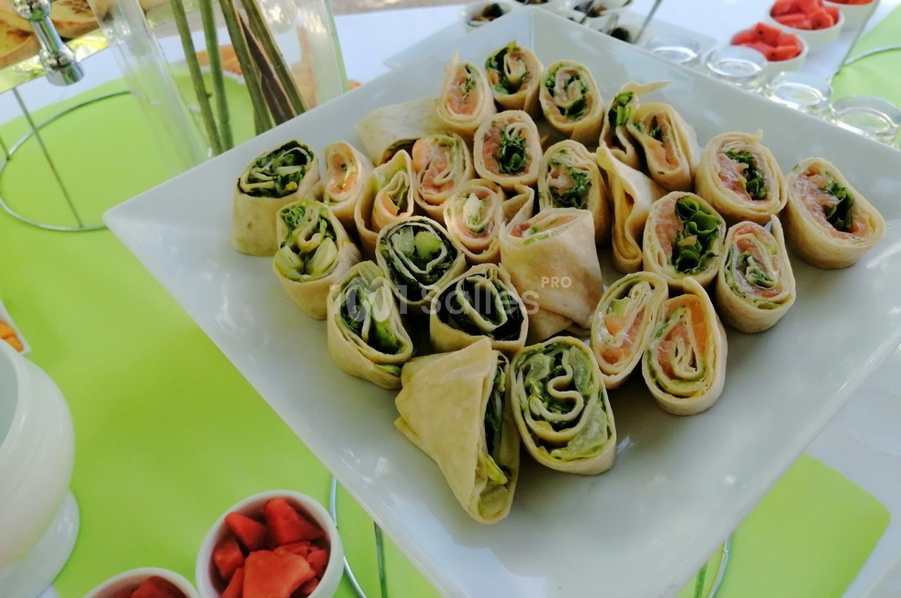 Plateau de wraps garnis de saumon, jambon et légumes, disposés sur une table avec des accompagnements.
