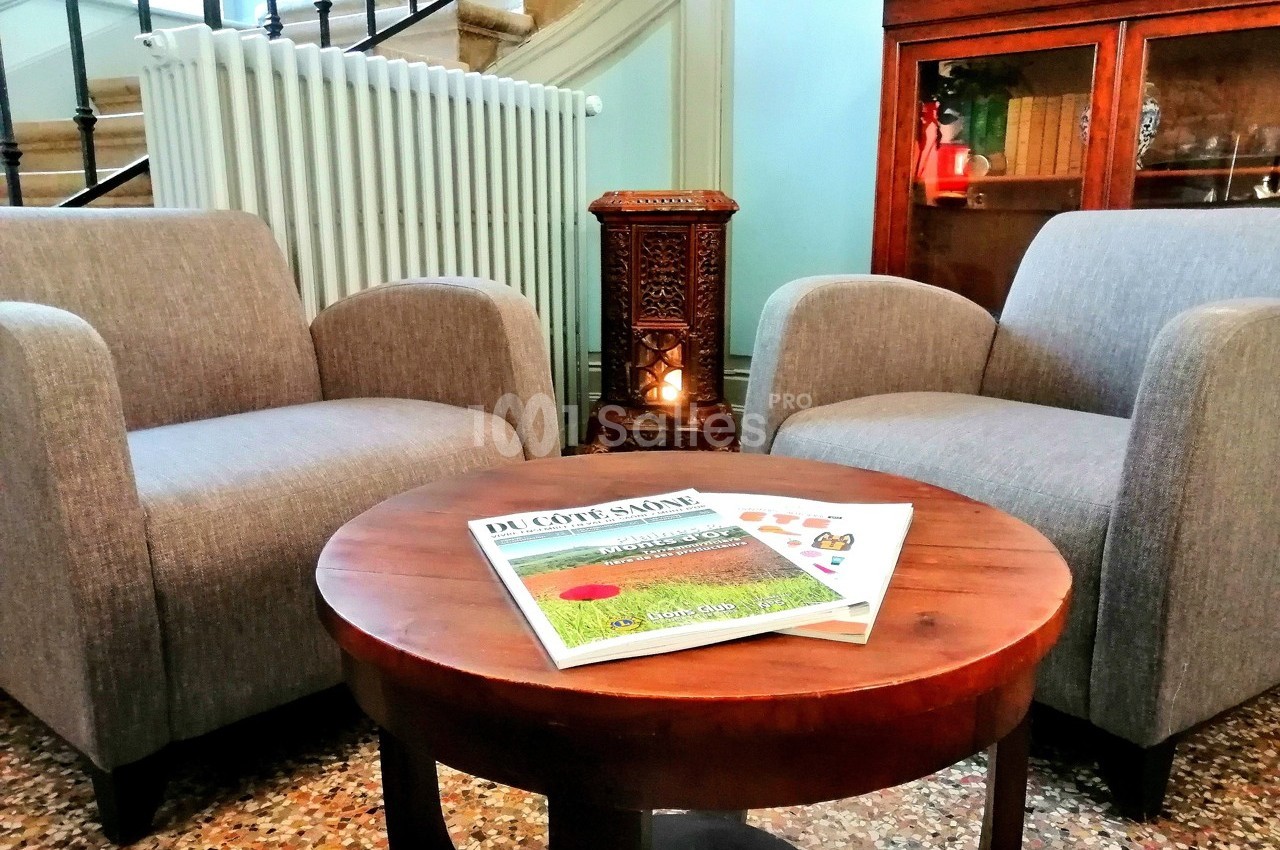 Deux fauteuils gris entourent une table ronde en bois avec des magazines, dans un salon au décor chaleureux.