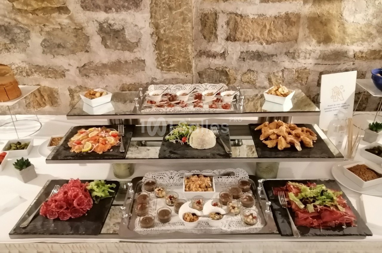 Buffet avec une variété de plats, incluant charcuteries, salades, desserts et amuse-bouches, présenté sur des plateaux.
