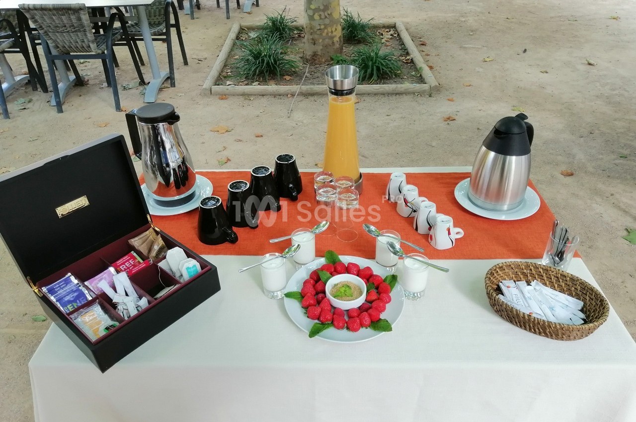 Table dressée en extérieur avec boissons chaudes, jus d'orange, fraises, condiments et accessoires de service.