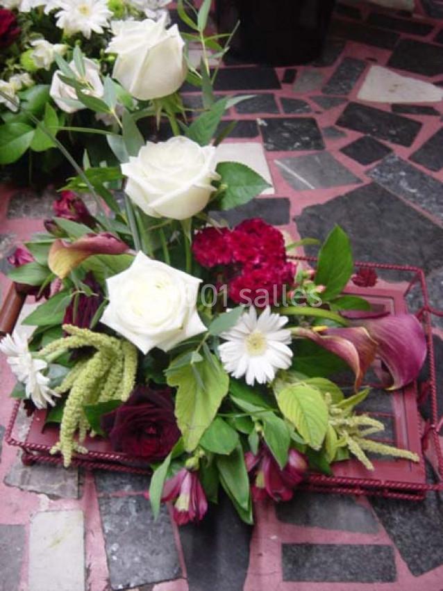Arrangement floral avec des roses blanches, des fleurs rouges et des feuillages verts sur un fond de carrelage.