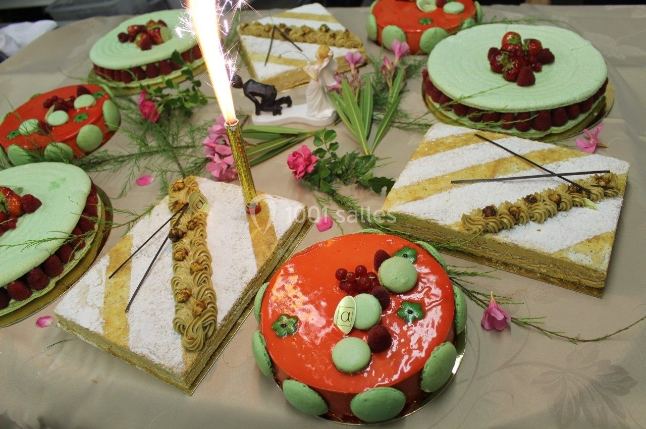 Assortiment de gâteaux décorés avec fruits, macarons et bougie allumée sur une table ornée de fleurs.