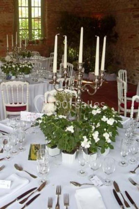 Tables élégamment dressées avec nappes blanches, chandeliers, fleurs blanches et couverts disposés pour un événement.