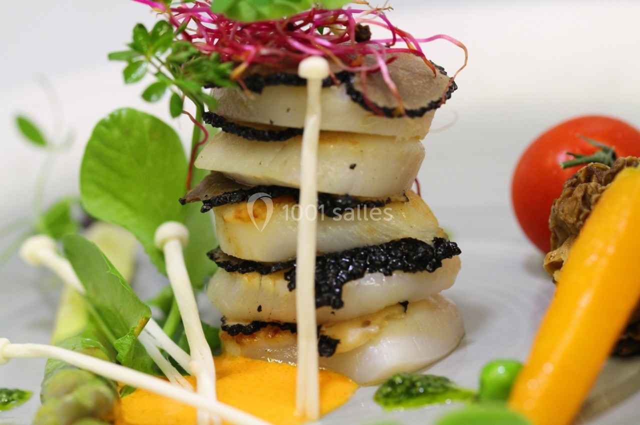 Assiette gastronomique avec des noix de Saint-Jacques, truffes, légumes colorés et sauce orange, présentée avec soin.