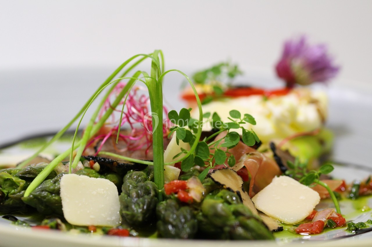 Assiette garnie d'asperges, copeaux de fromage, truffes, herbes fraîches et fleurs comestibles.