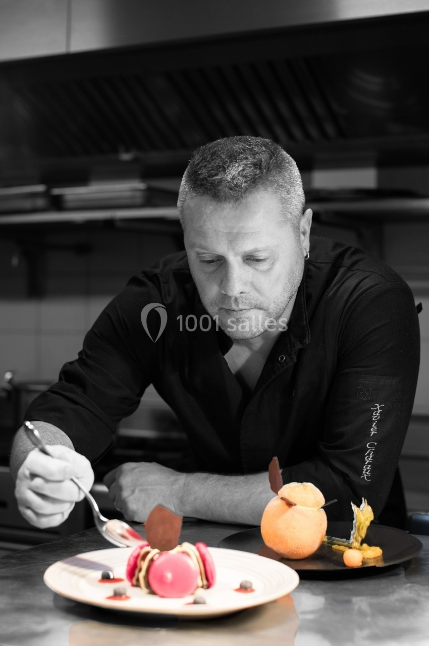 Un chef pâtissier concentré décore un dessert coloré dans une cuisine professionnelle.