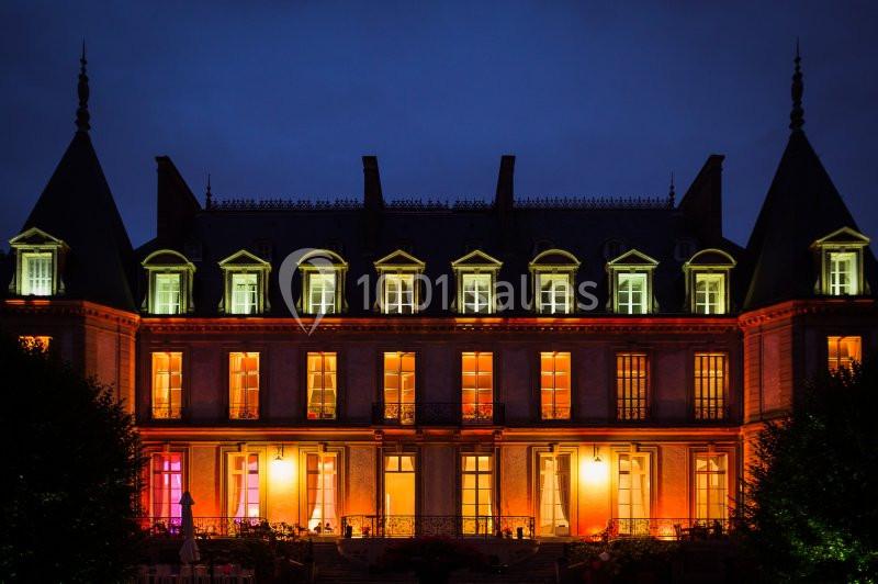 Façade d'un château éclairée par des lumières colorées, photographiée de nuit.